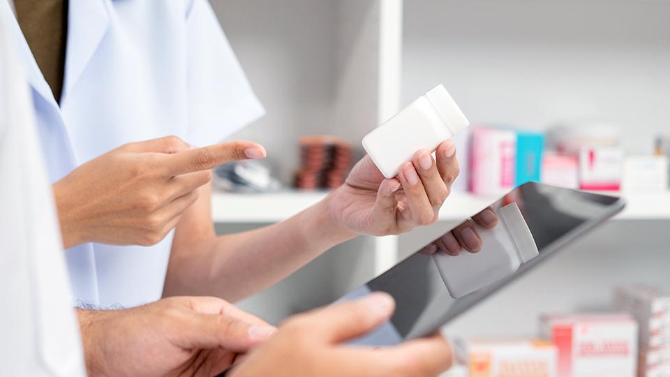 The hands of two students; one is holding a pill bottle and one is holding a tablet.