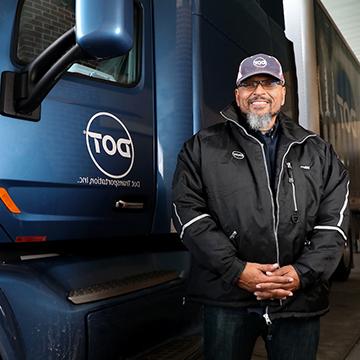 A student wearing a proud smile stands next to the cab of a commercial truck.