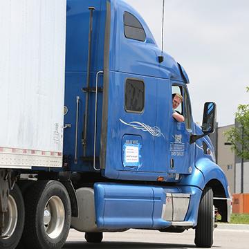 A male CDL student looks out of the window of a semi truck trailer 