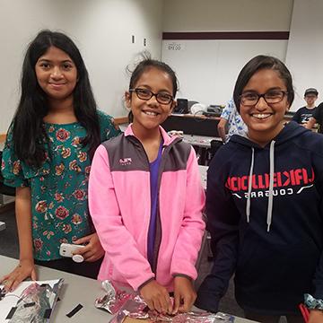 three female students stand smiling at the camera