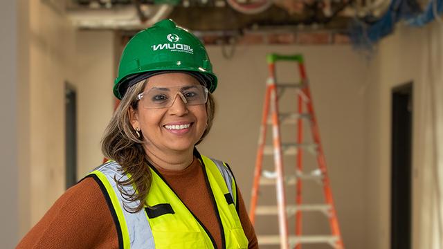 Ana Linz Perdigao in a hard hat and construction vest with a ladder in the background